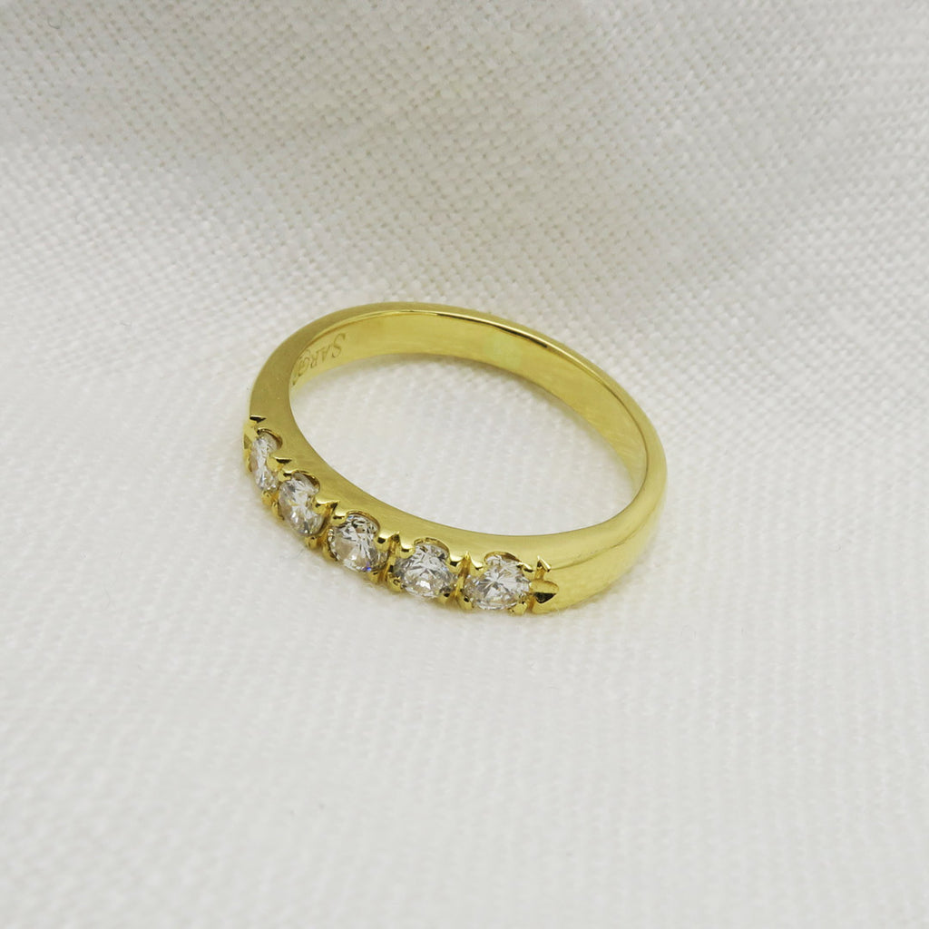 side view of yellow gold wedding ring set with five white diamonds. White background. 