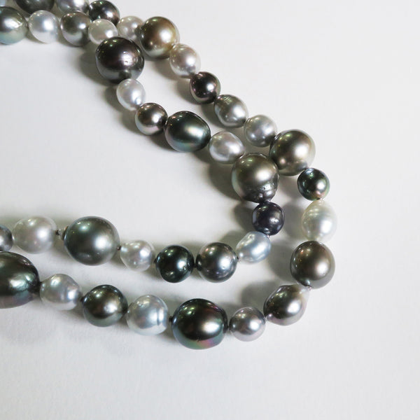 Close up pearl strand silver grey black Tahitian south sea pearls. White background. 